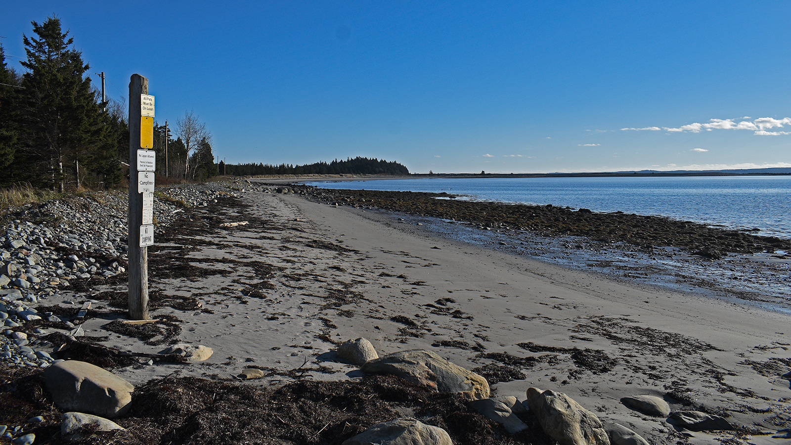 A beach on McNabs Island nearby Garrison Pier. On it are signs on a wooden post that read "no camping" and "no campfires".