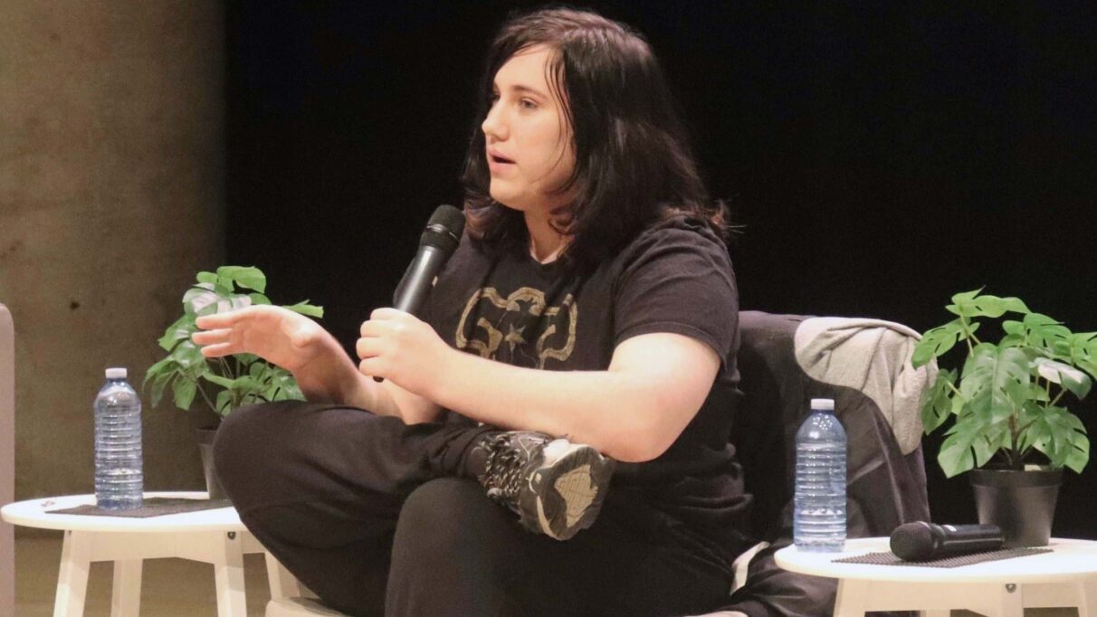Young person sitting in a chair and holding a microphone at a panel.