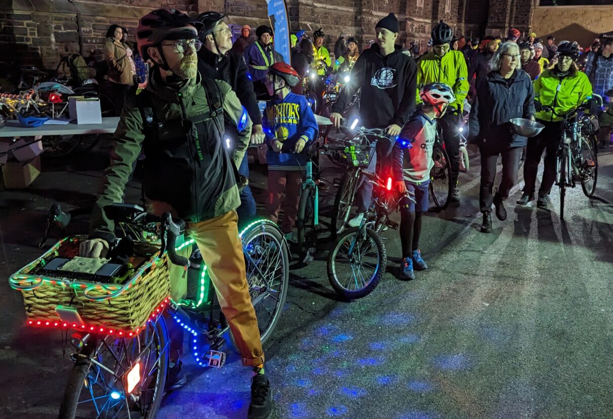 Halifax cyclists gather in a church parking lot with their lit up bikes at night.