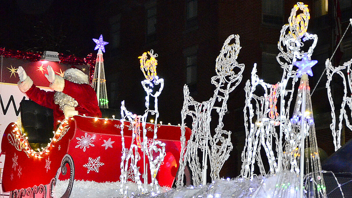 Santa Claus sits in his sleigh pulled by light up reindeer while waving to the crowd.
