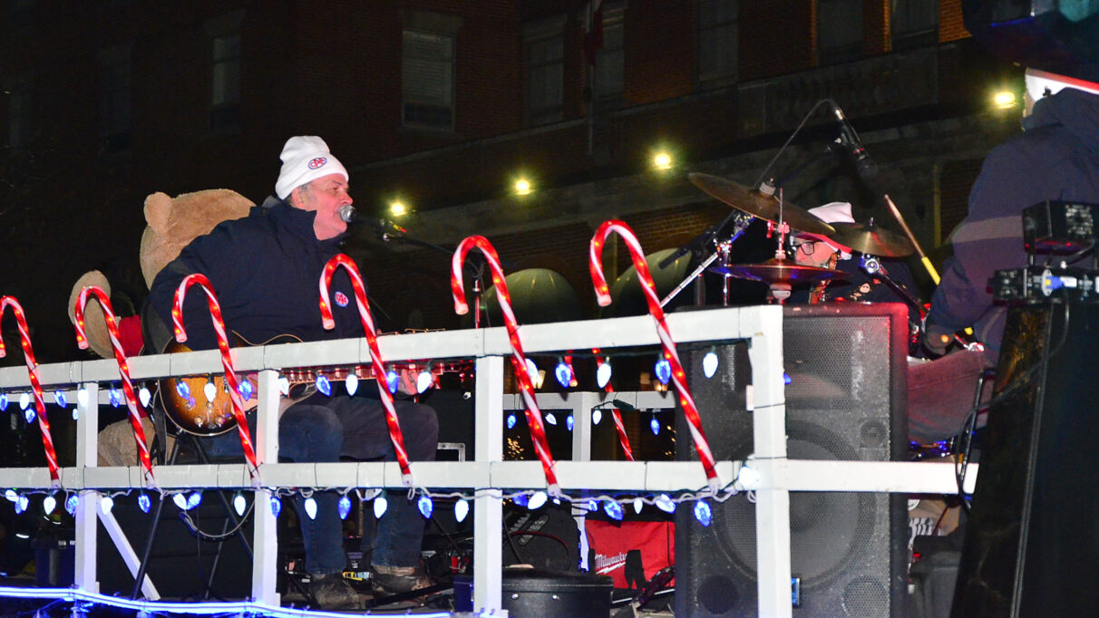 A live band, including a guitar, singer and drums plays on top of a parade float lined with big plastic candy canes.
