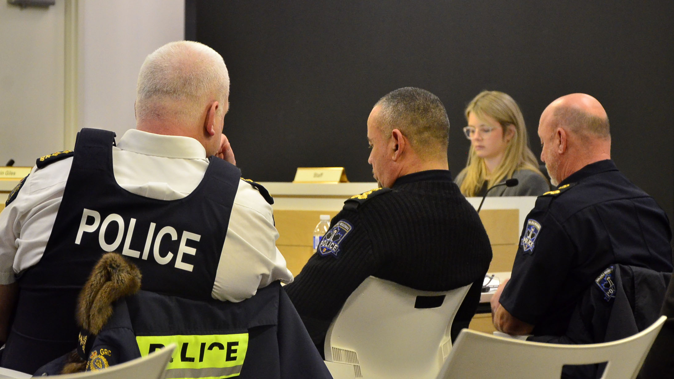 Three police officers sit in chairs at a board meeting.
