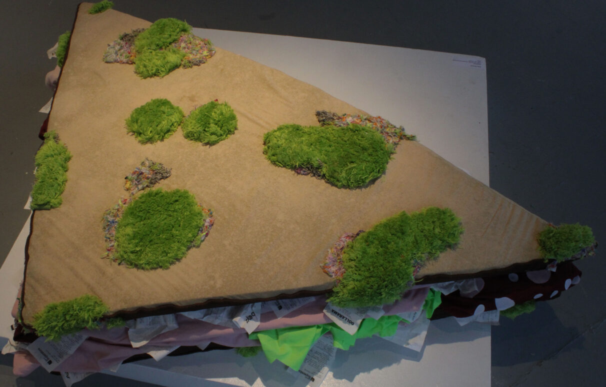 An overhead shot of an over-sized sandwich made out of foam mats, bed sheets, reusable grocery bags and bathmats.