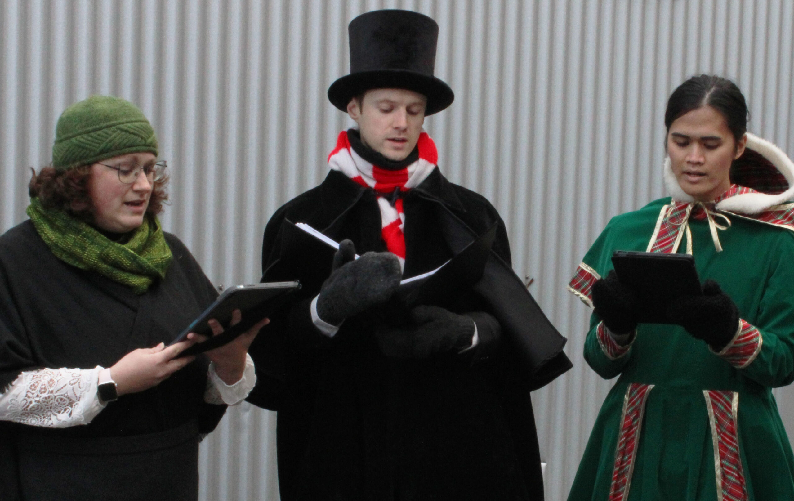 Three people standing in line horizontally, reading music as they sing.