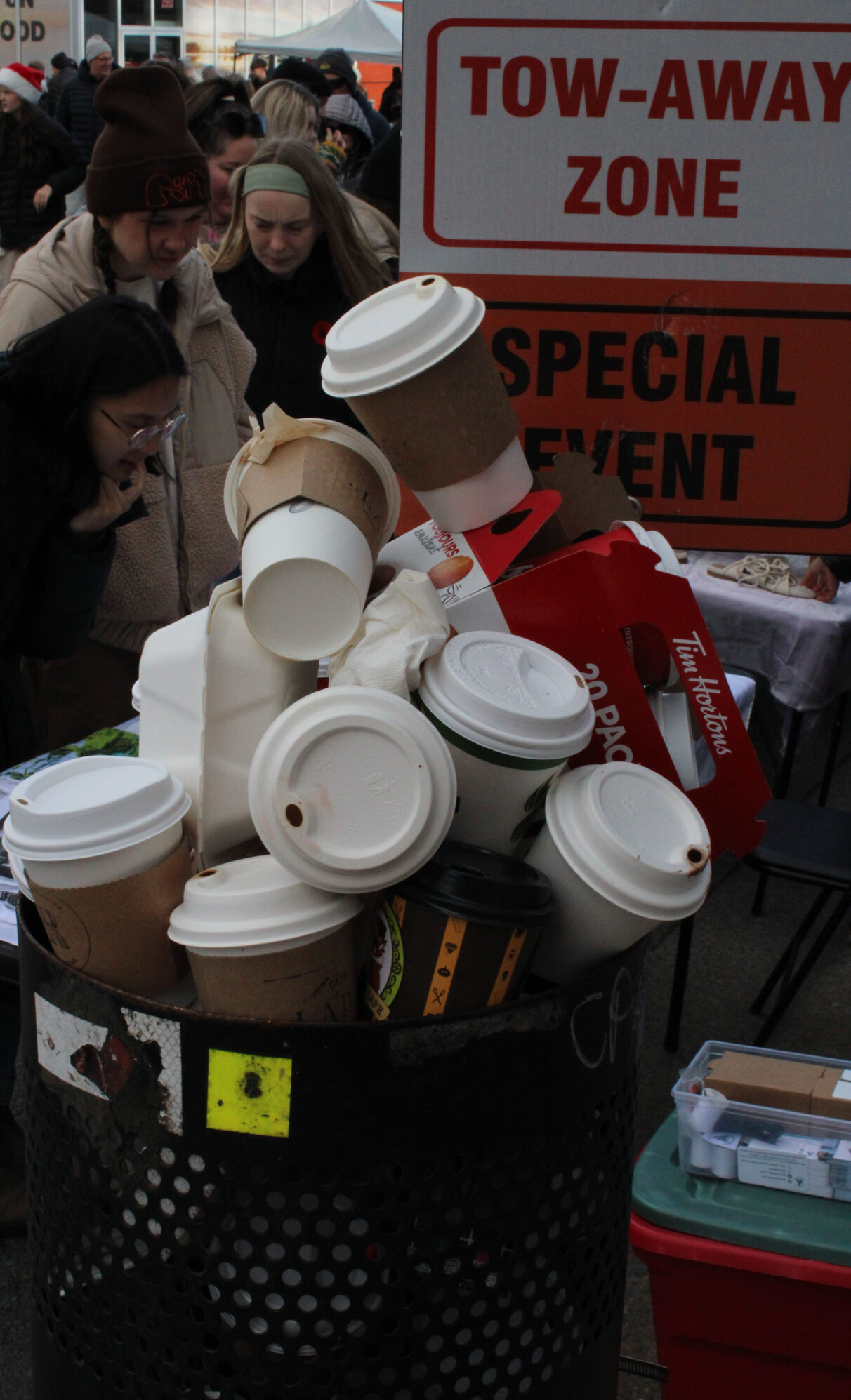 A garbage can overflows with coffee cups next to signs that say "Tow-Away Zone" and "Special Event."
