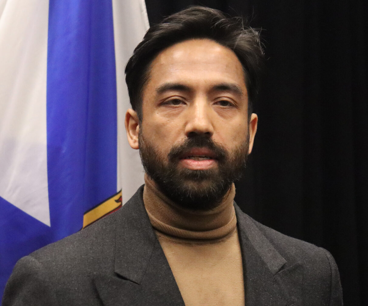 A man with beard standing in front of Nova Scotia flag.