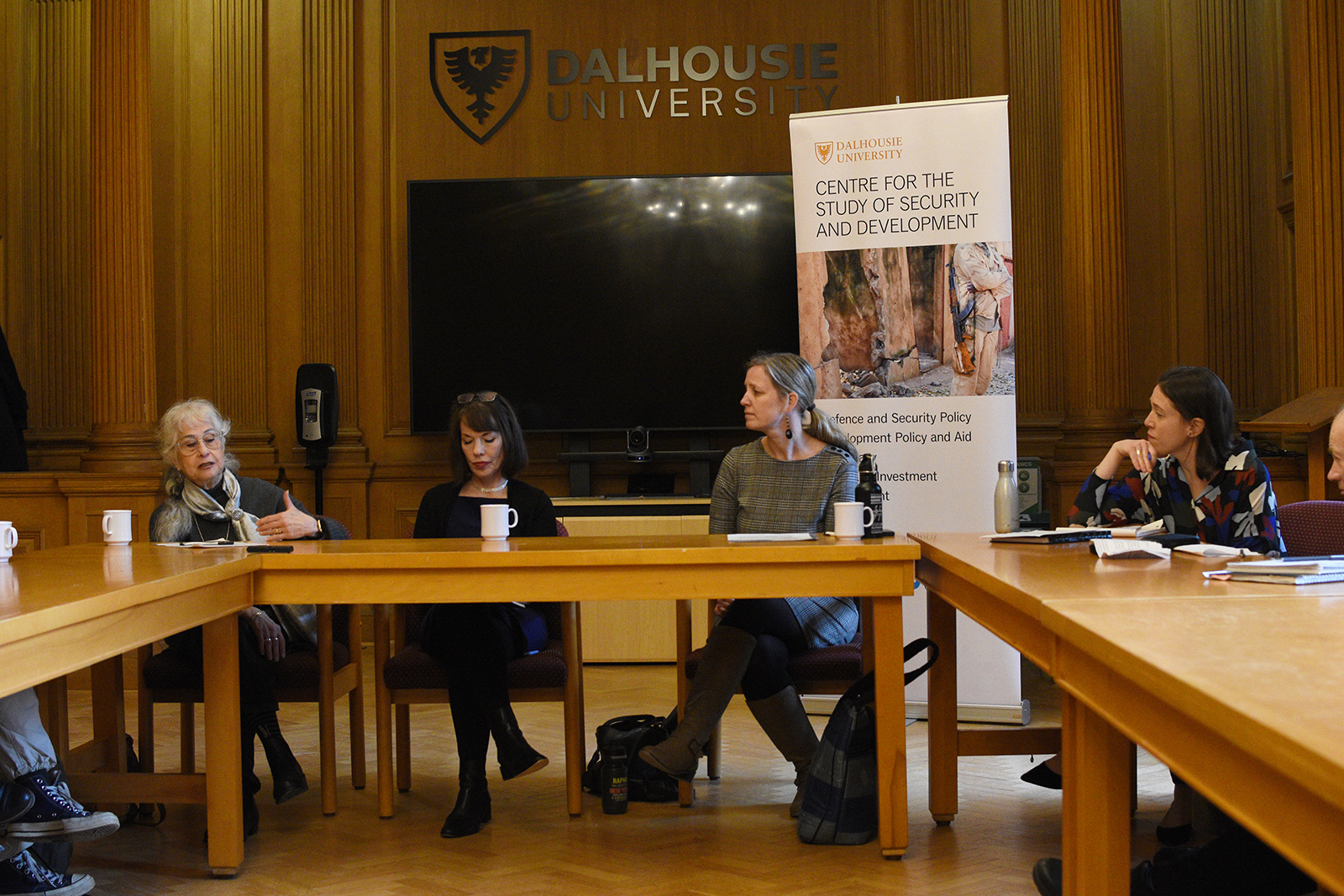A panel of experts sit by large tables and discuss in a University room.