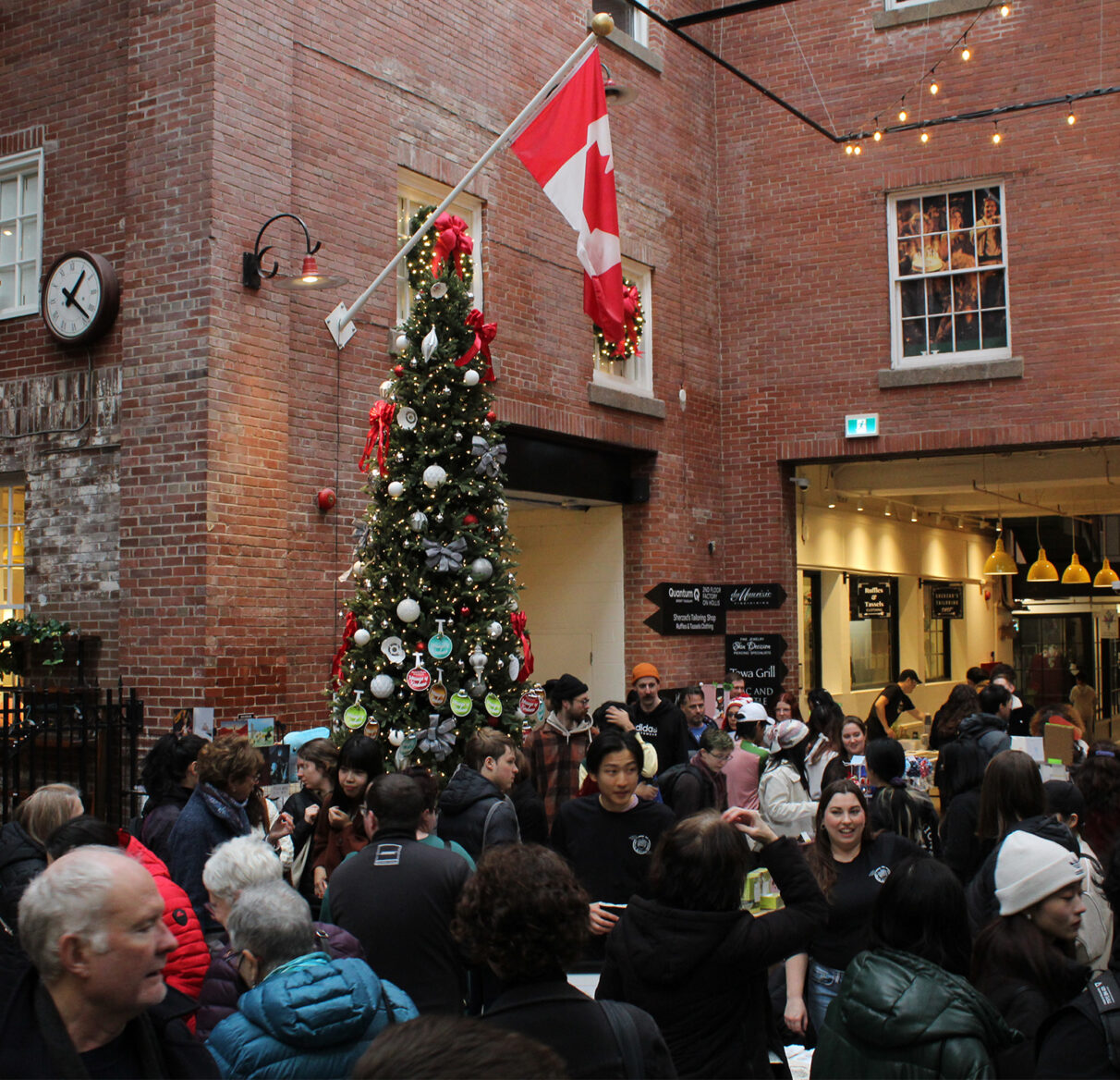 A crowd of people in a room standing under a Christmas tree and Canadian flag.