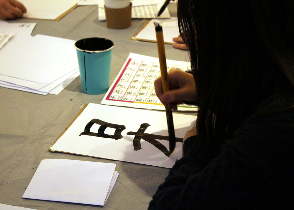 A person painting Japanese characters on a sheet of paper.
