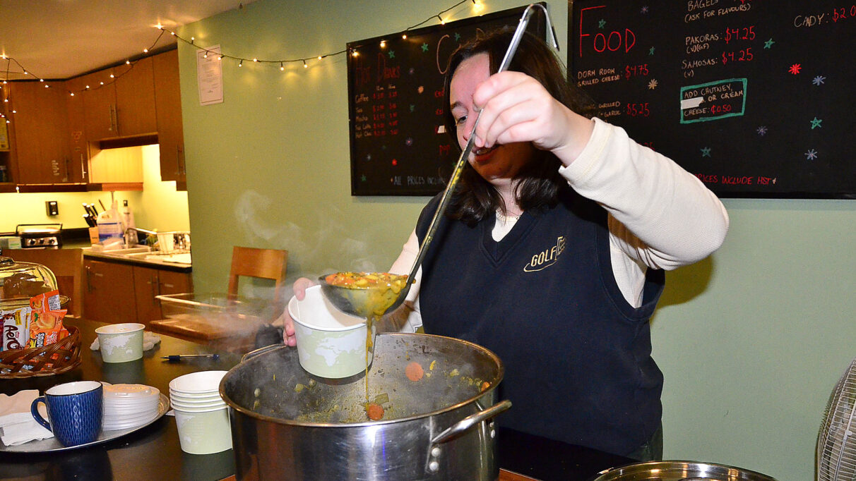 A Galley staff member ladles steaming soup into a bowl.