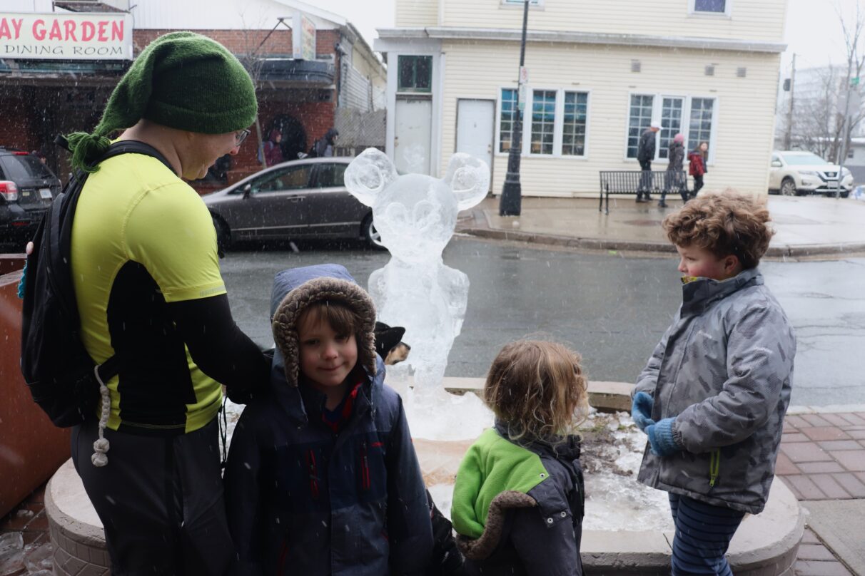 Man and three children stand in front of an ice sculpture shaped like Mickey Mouse.