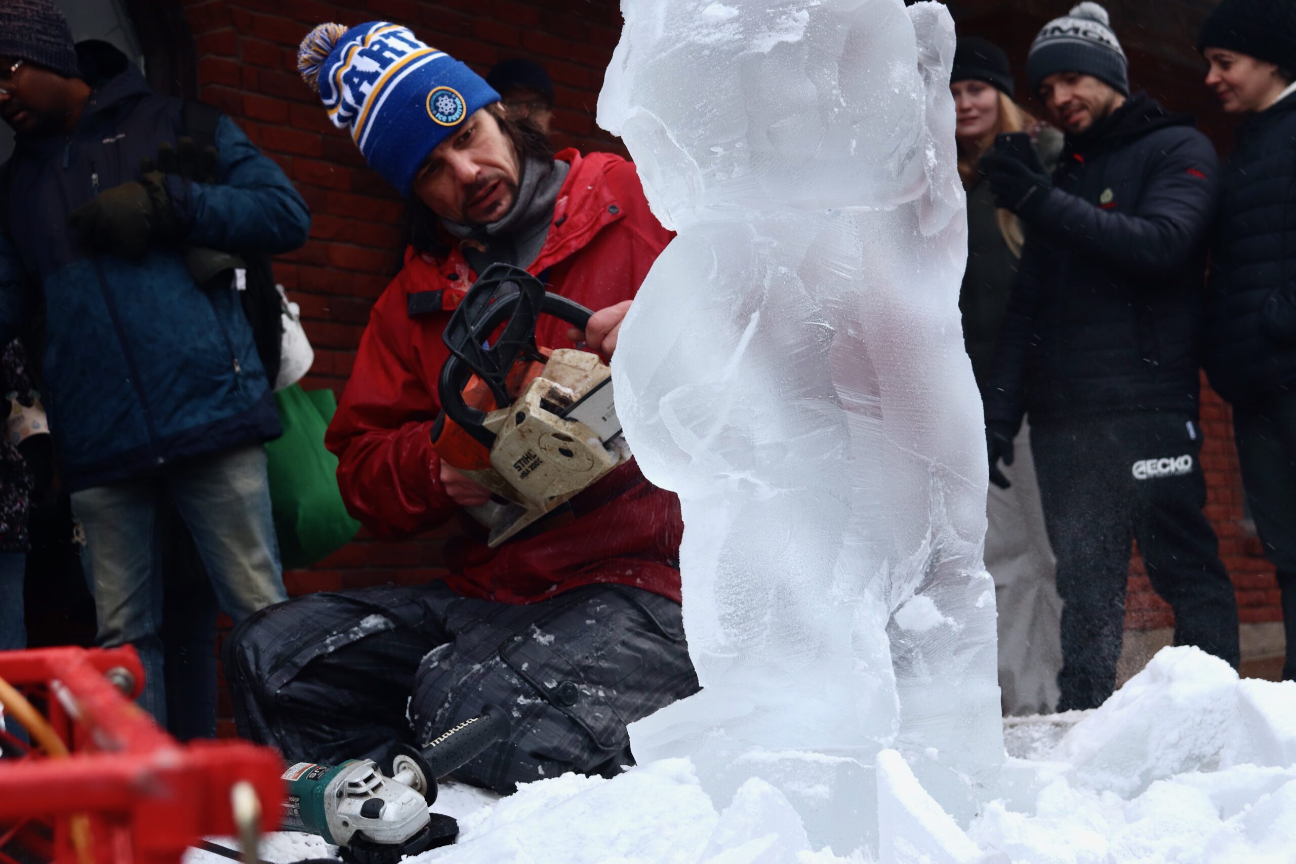 Kneeling man uses chainsaw to carve an ice sculpture.