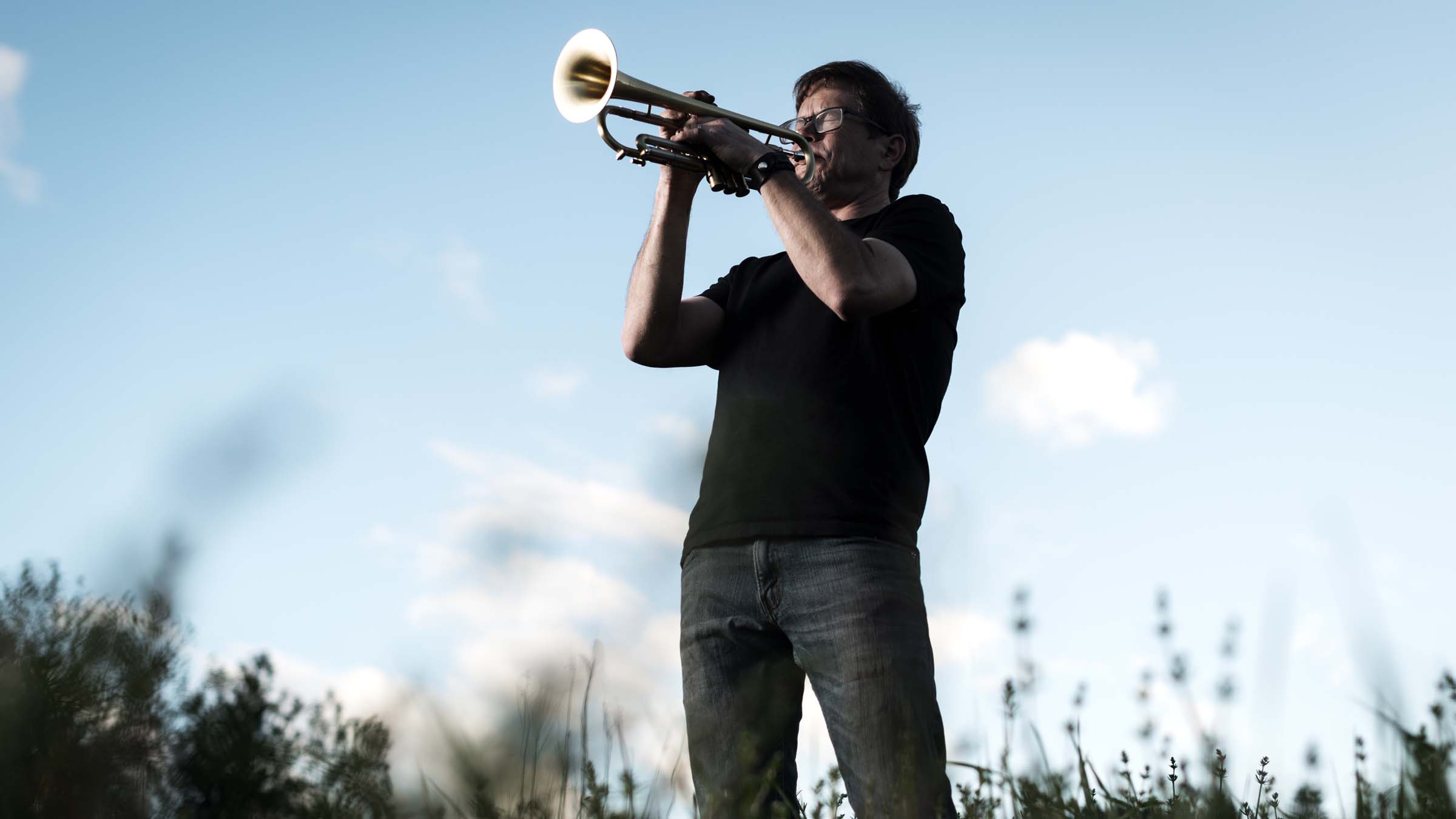 A man stands in a field playing the trumpet.