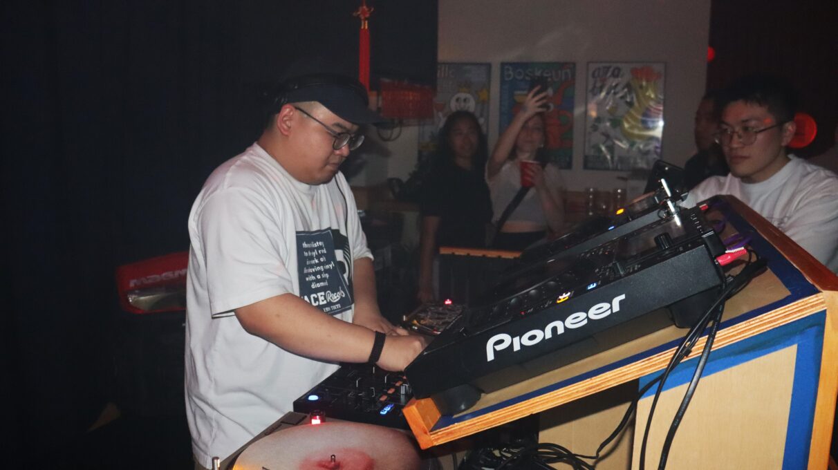 A man plays the DJ controller, and other people look at him and take pictures.
