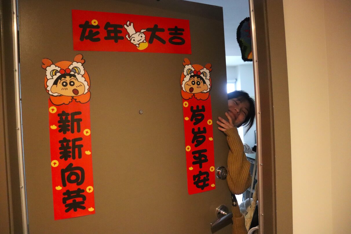 A woman leans on the door with chunlian taped on it.