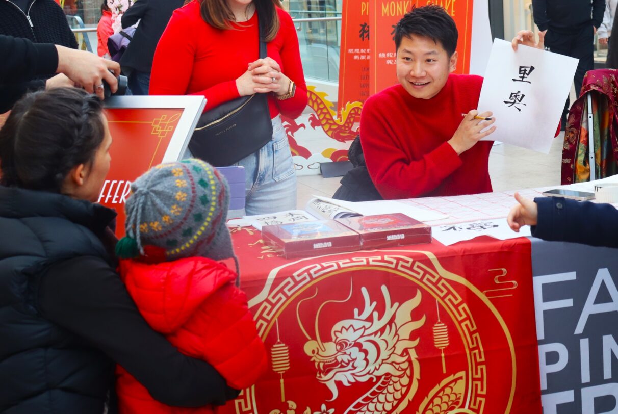 A man in red clothes holds up a piece of paper with "Li Ao" written on it, which is the English name Leo in Chinese.