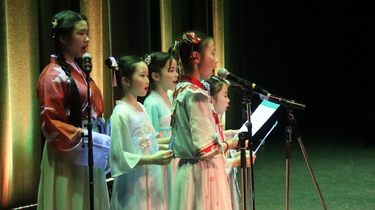 A group of children wearing Hanfu face microphones and speaking.