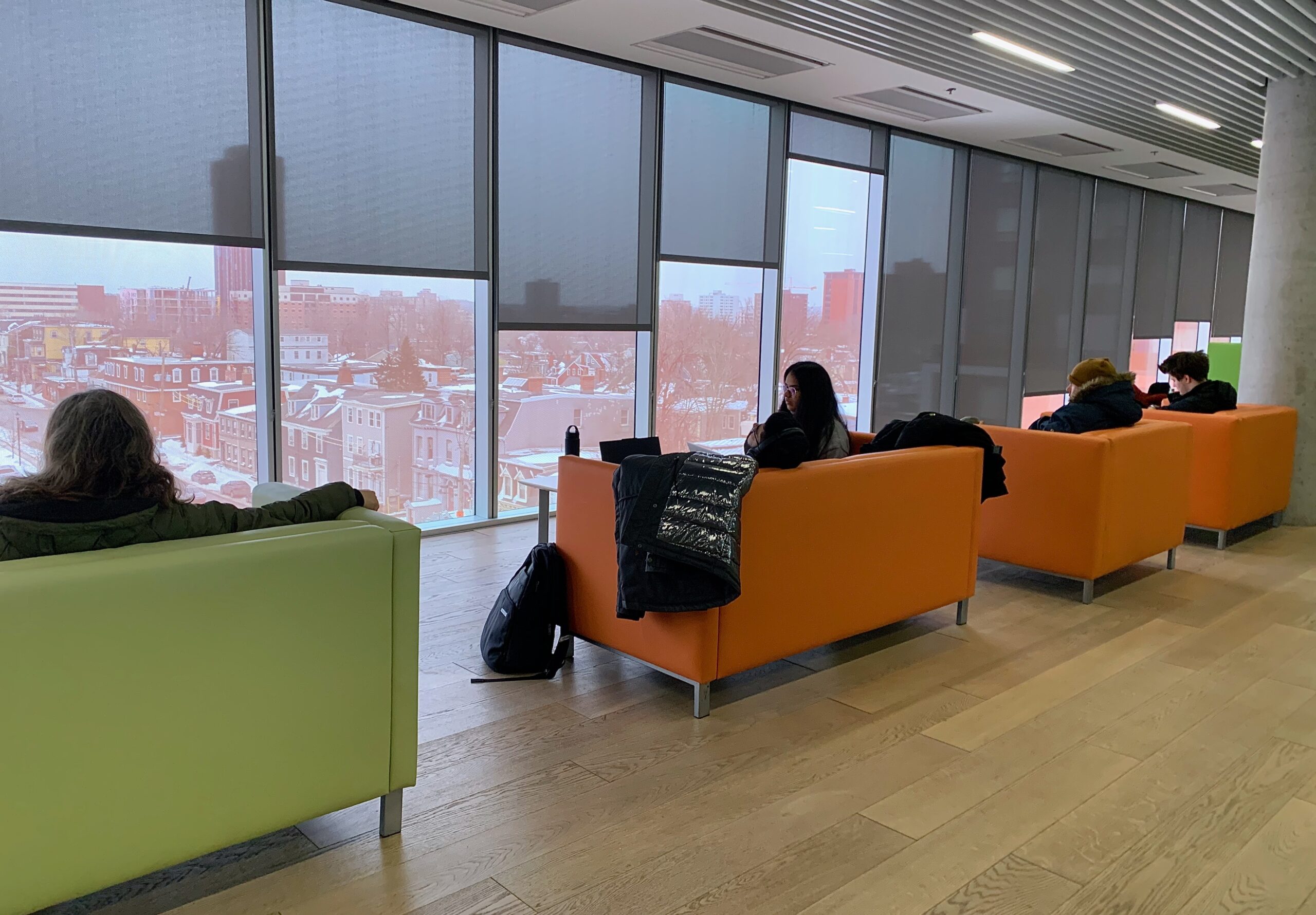 Four people sit on orange and green chairs near a window at the Halifax Central Library