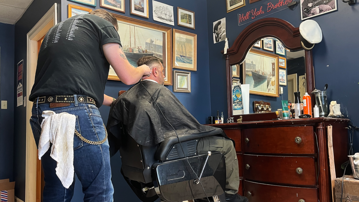 A barber giving a man a haircut while sitting at the barber's chair.