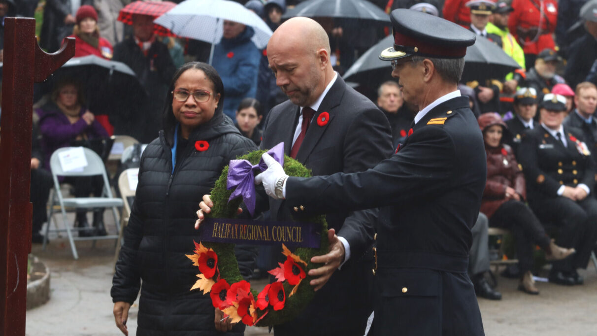 a man in military uniform hands another man a commemorative wreath