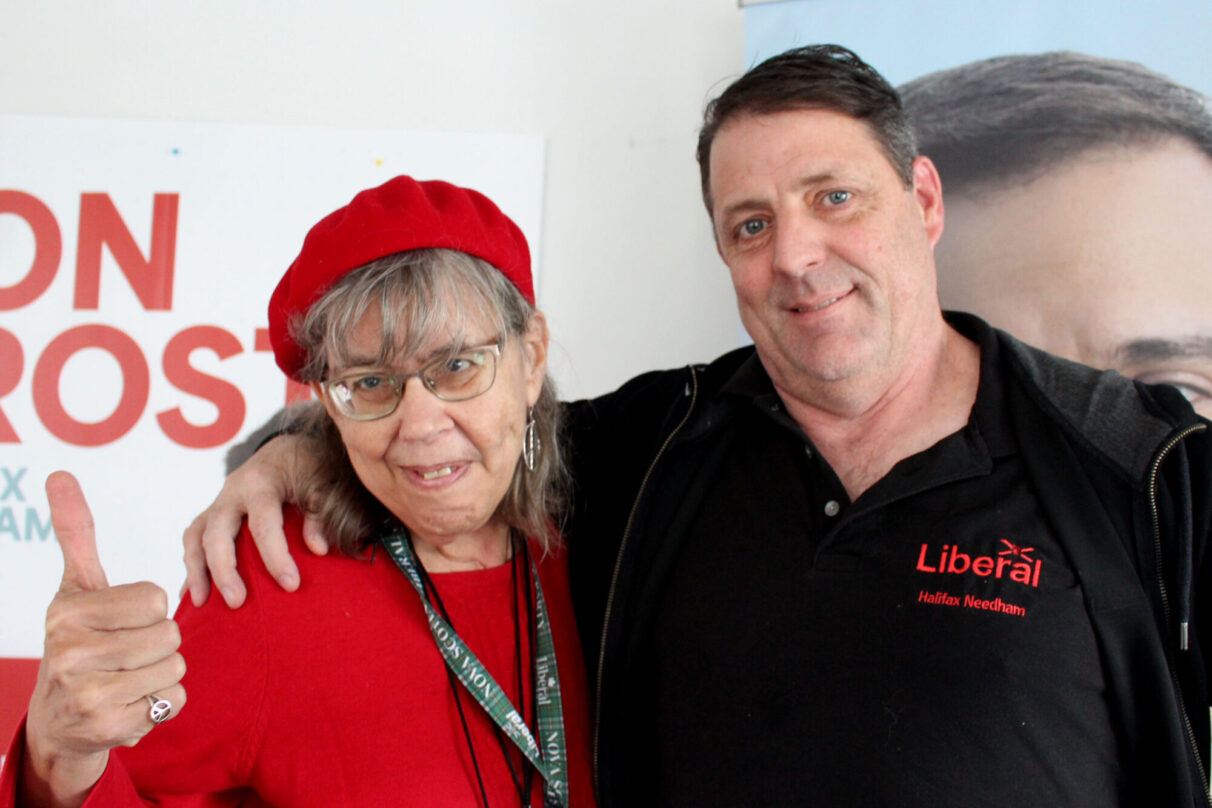 A man and woman pose for a picture. The woman wears an all red outfit and the man wears a black sweater.