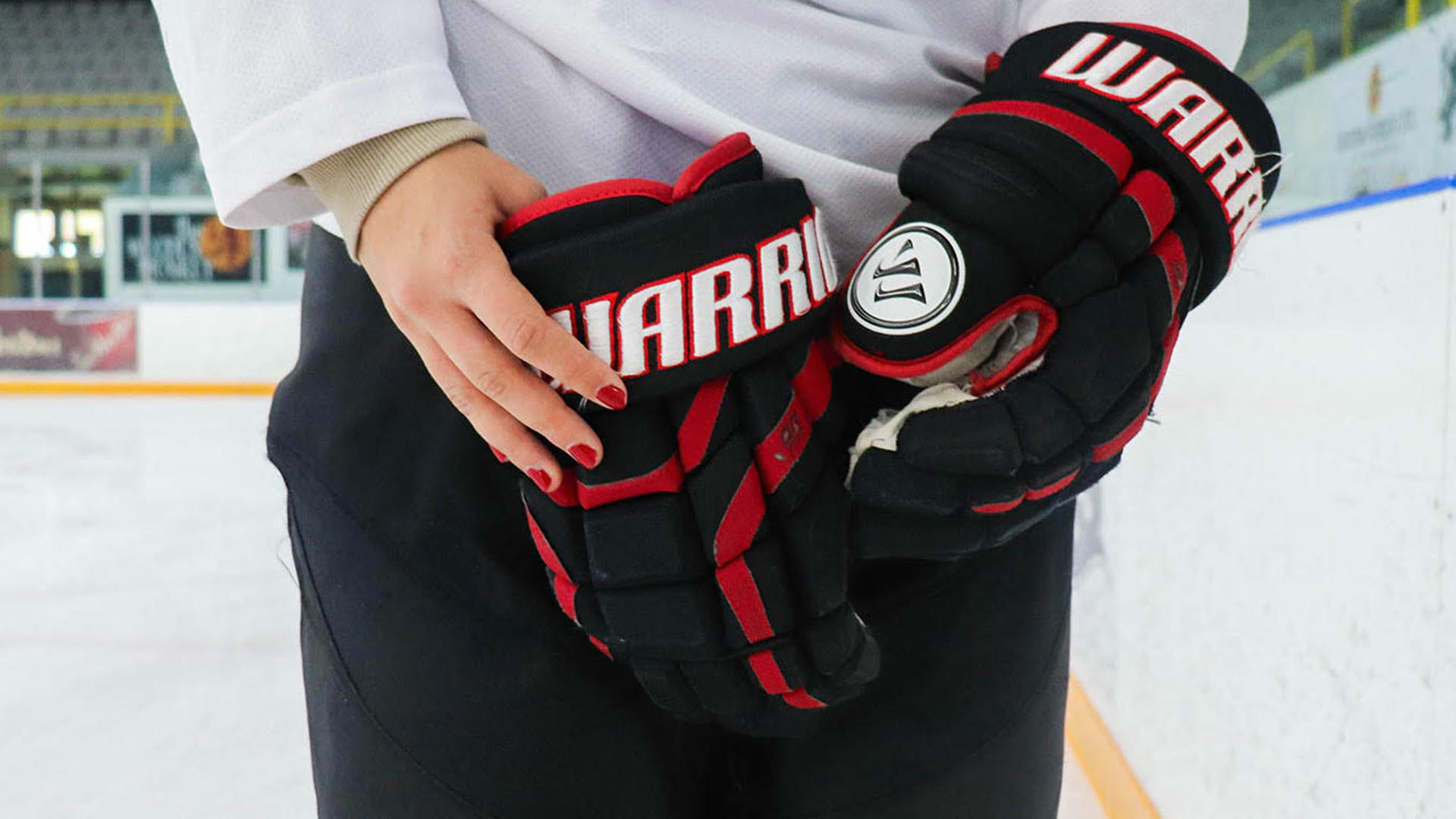 A woman putting on hockey gloves on the ice.