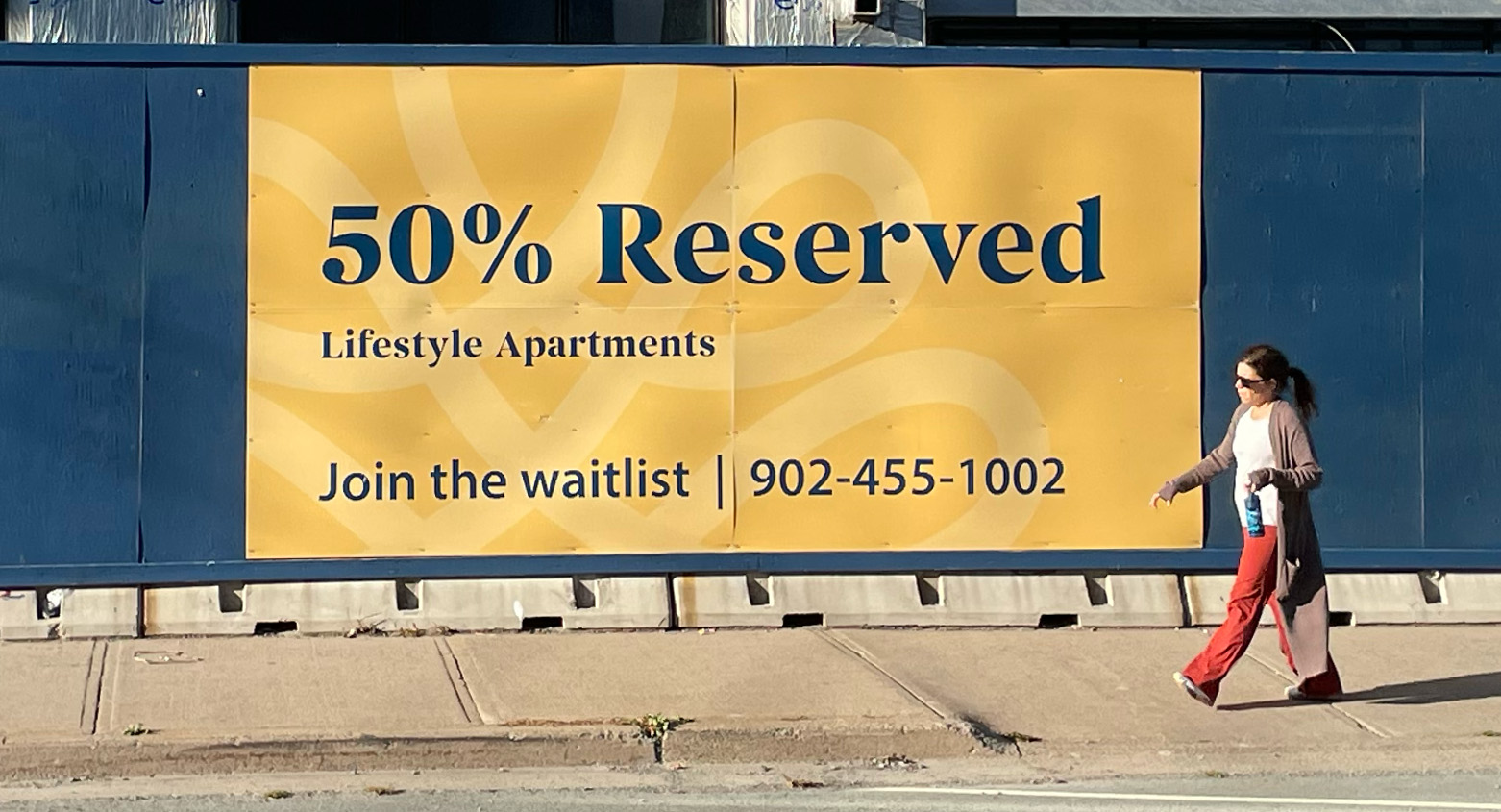 A woman walking past a sign for a new apartment building in Halifax.