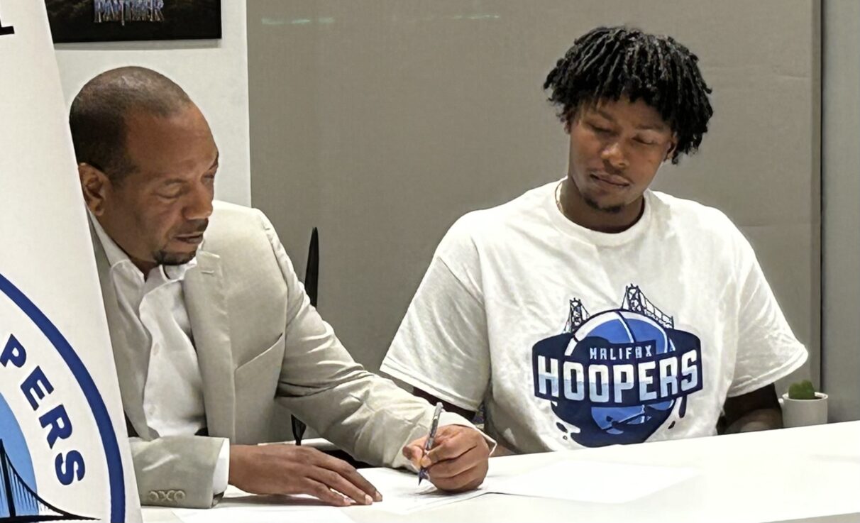 A Halifax Hooper player and owner sit at a desk to sign a contract