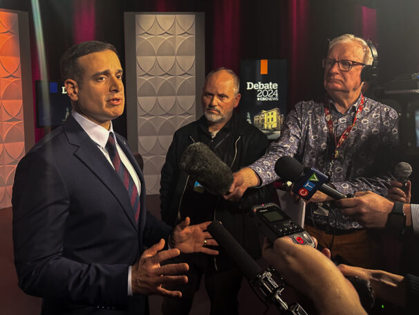 A man answering questions from journalists in front of microphones and cameras.