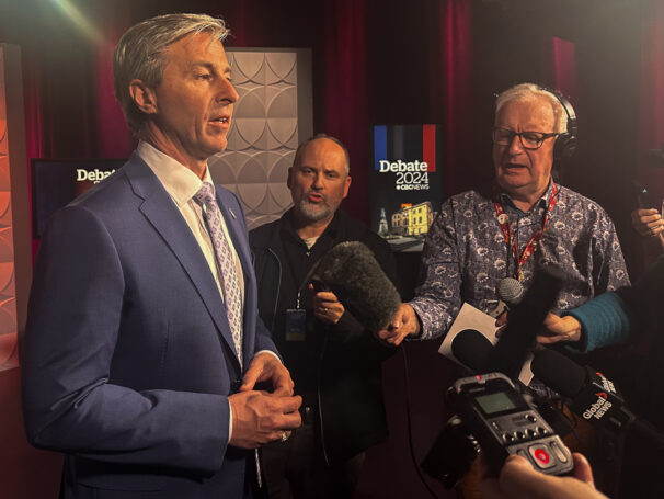 A man answering questions from journalists in front of microphones and cameras.