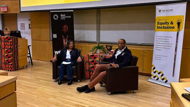 A woman and man seated having a conversation in an auditorium.