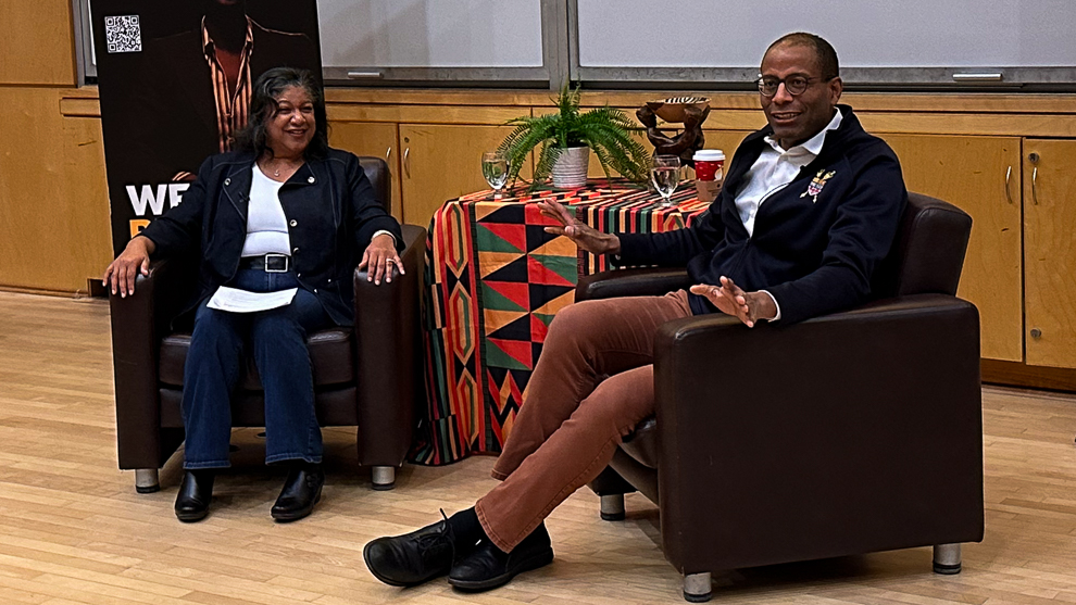 A woman and man seated having a conversation in an auditorium.