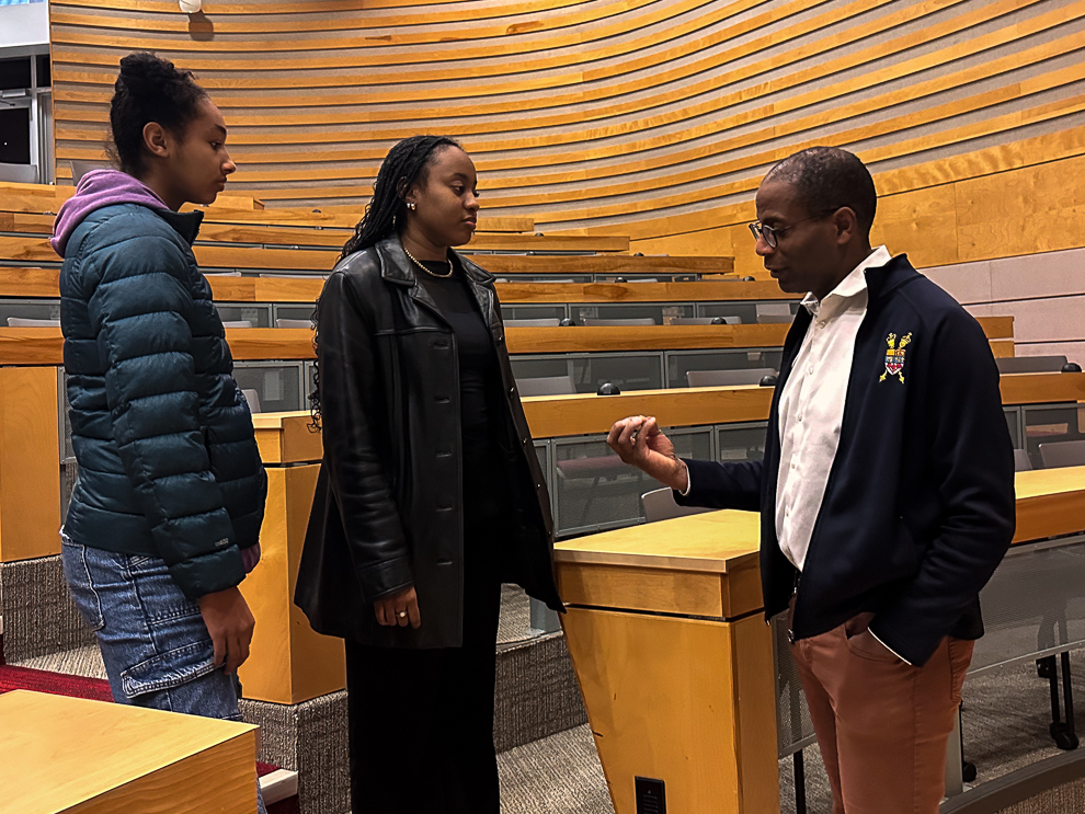 Two female students having a conversation with a man in a auditorium