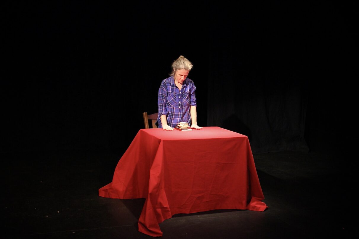 A woman stands at a table with a cup and a book.