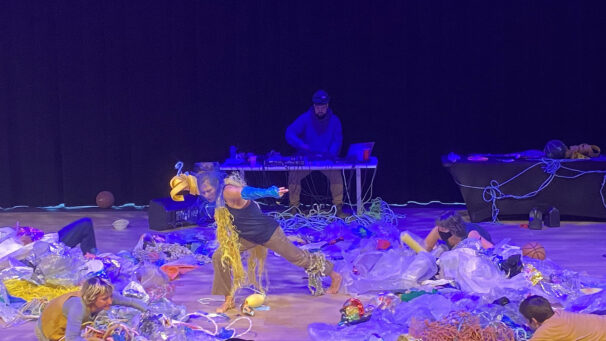 Three dancers crawling in plastic waste and one dancer covered in plastic standing in the centre