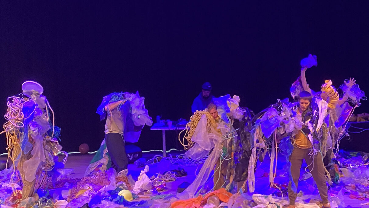 Five dancers covered in and surrounded by plastic waste.