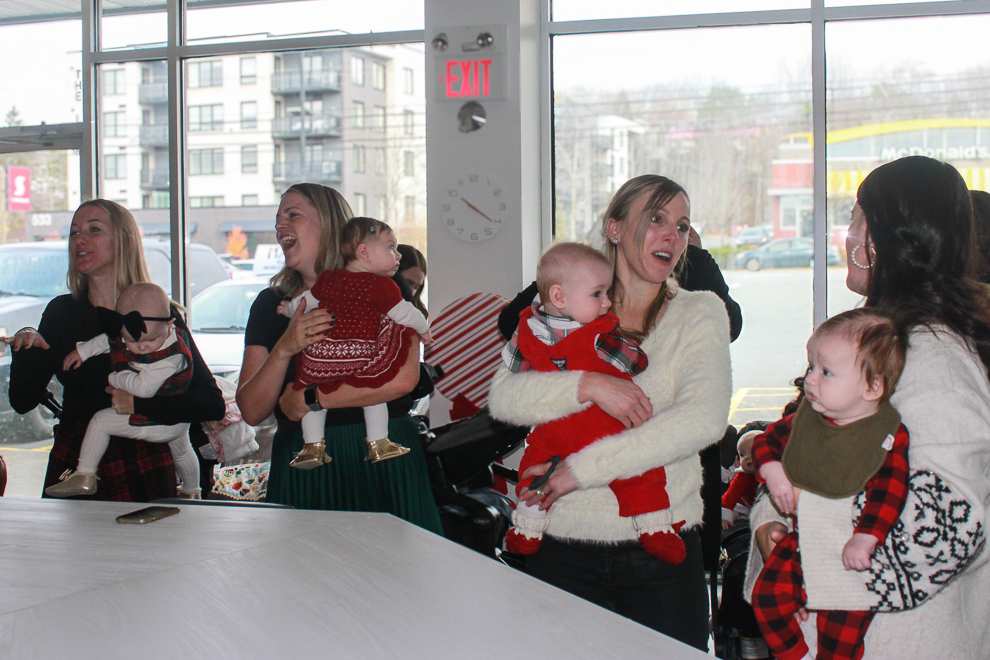 A group of moms standing at a counter holding their babies and converting with one another.