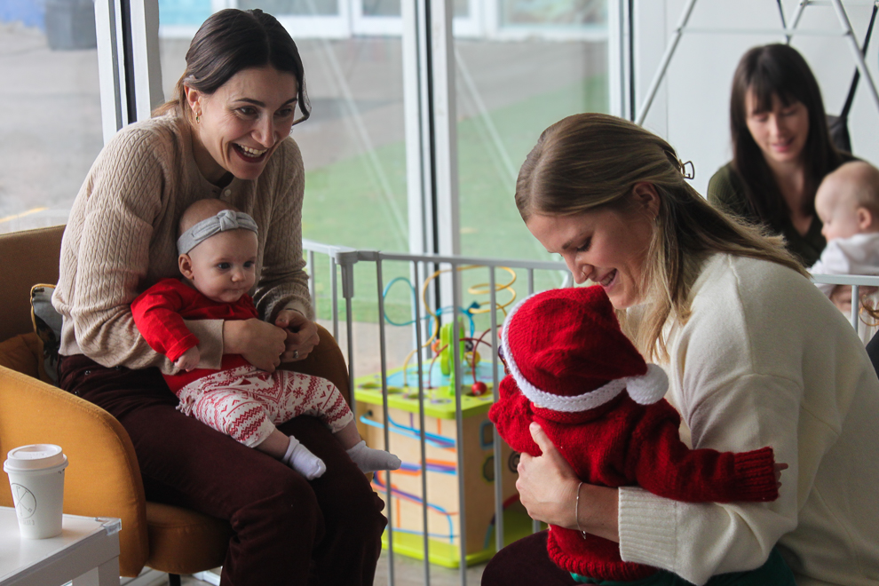 Two moms holding their babies in a play room.