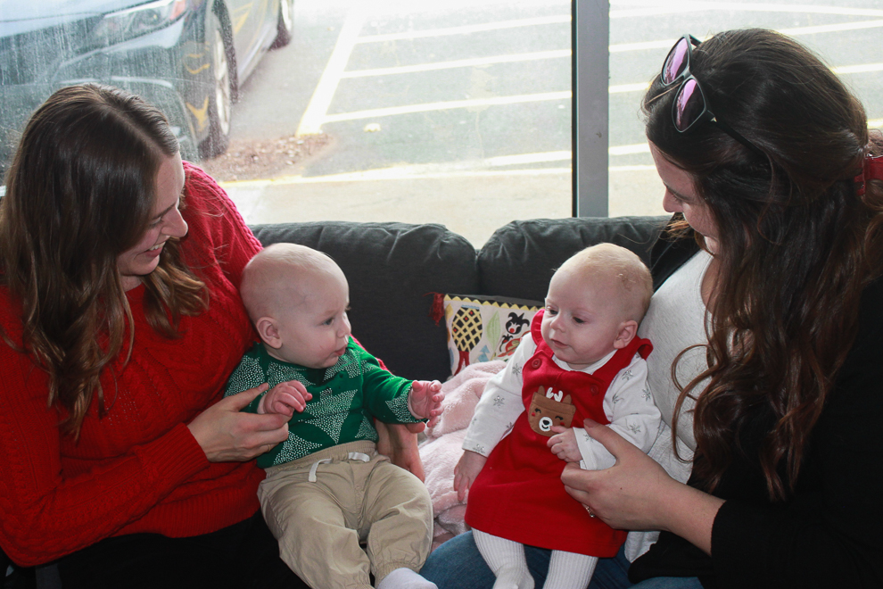 Two moms sitting on a couch with their babies.