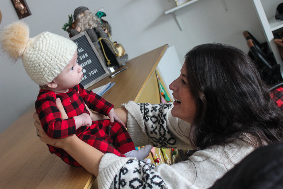 A mom holding propping her baby on a table and looking at him affectionatley.