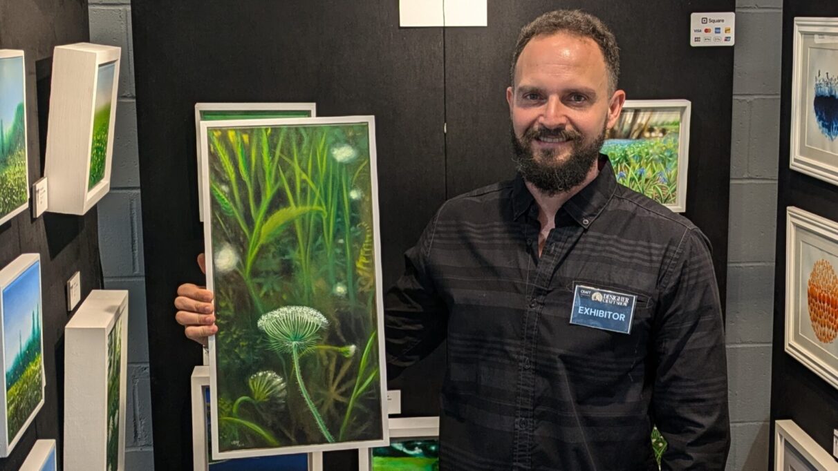 Jose Urbay stands in his booth holding one of his Queen Anne's Lace paintings