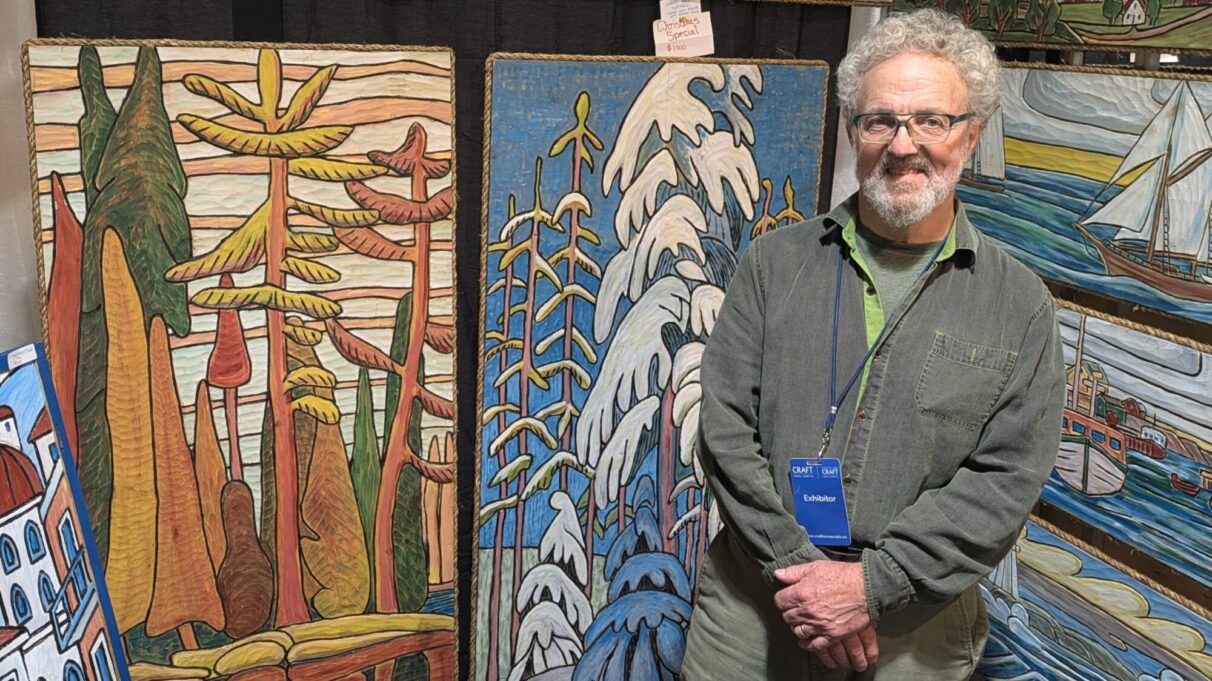 Brian Reid stands with with his painted wood carvings