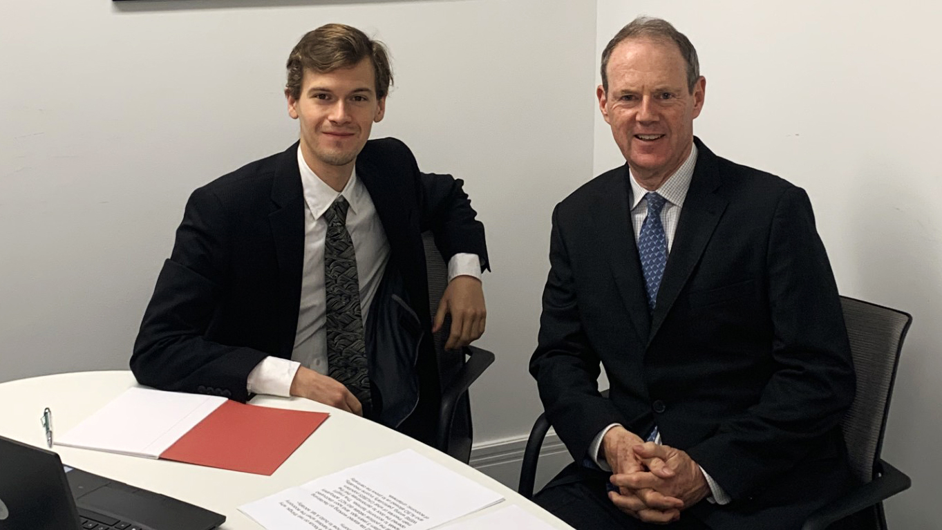 two men in suits sit behind a desk