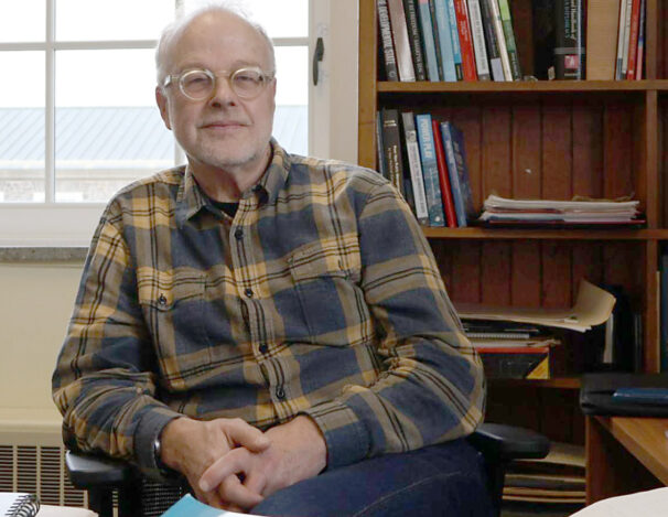 Man sits with hands crossed in front of a bookcase