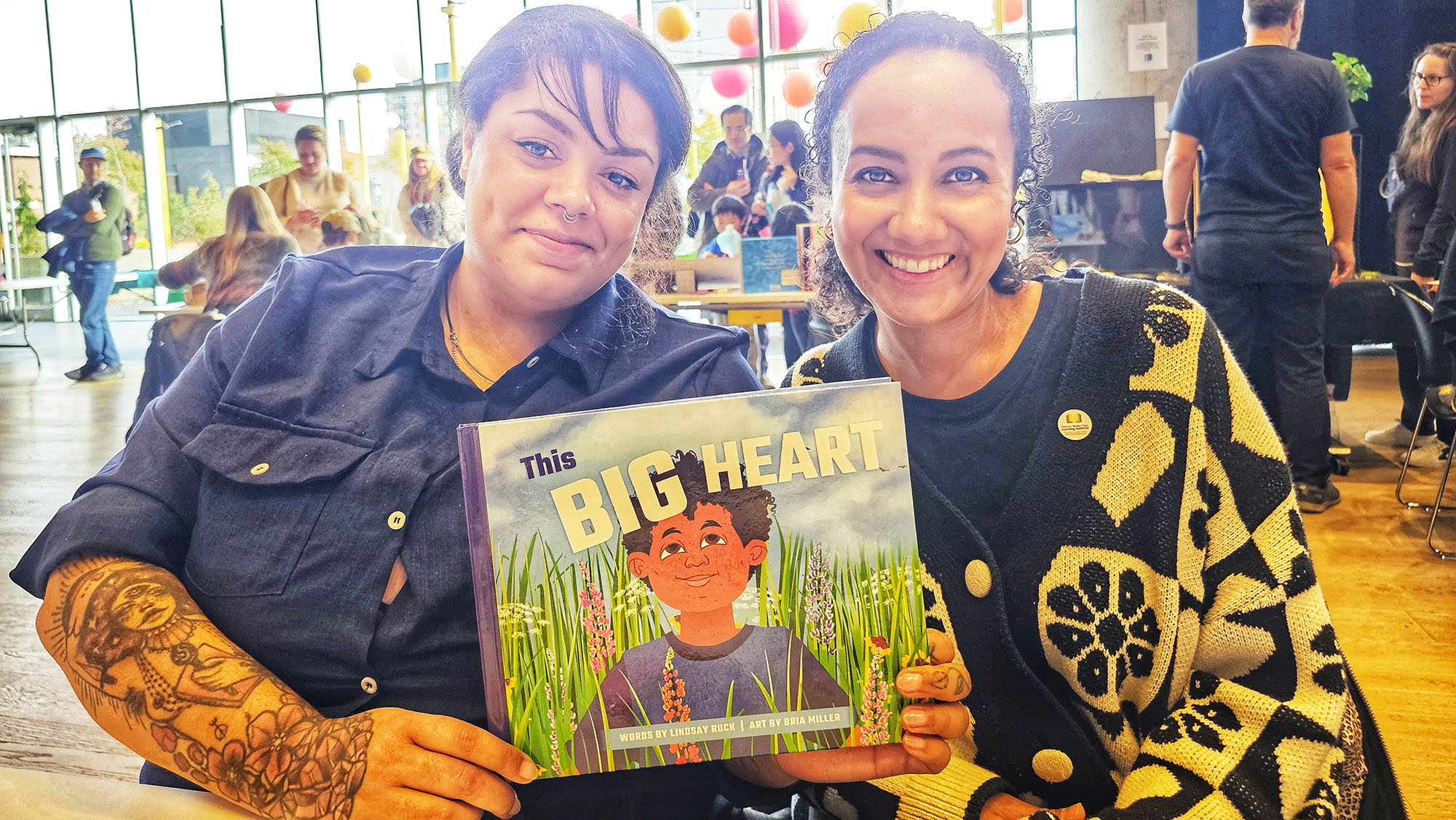 Two ladies smiling into the camera, holding a book.