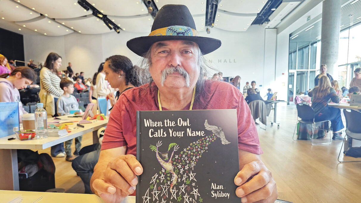 A man with a bowler hat, holding up a book.