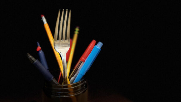 A fork and pens inside a glass jar.