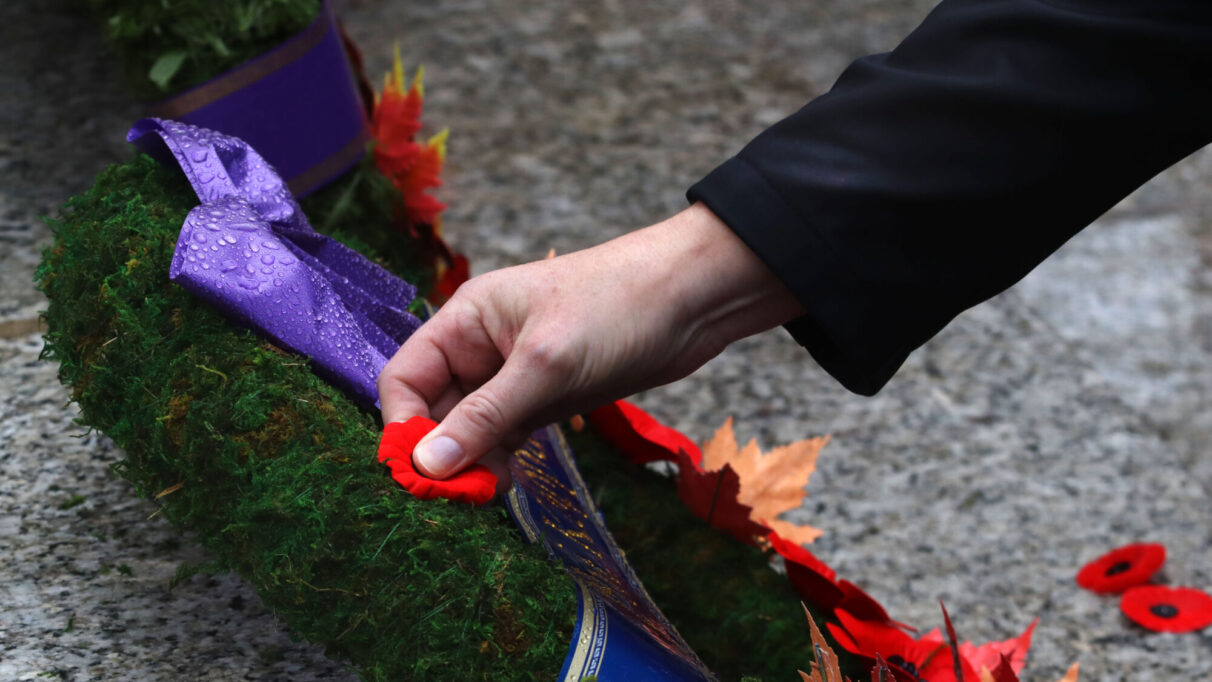 a hand pins a poppy to a wreath