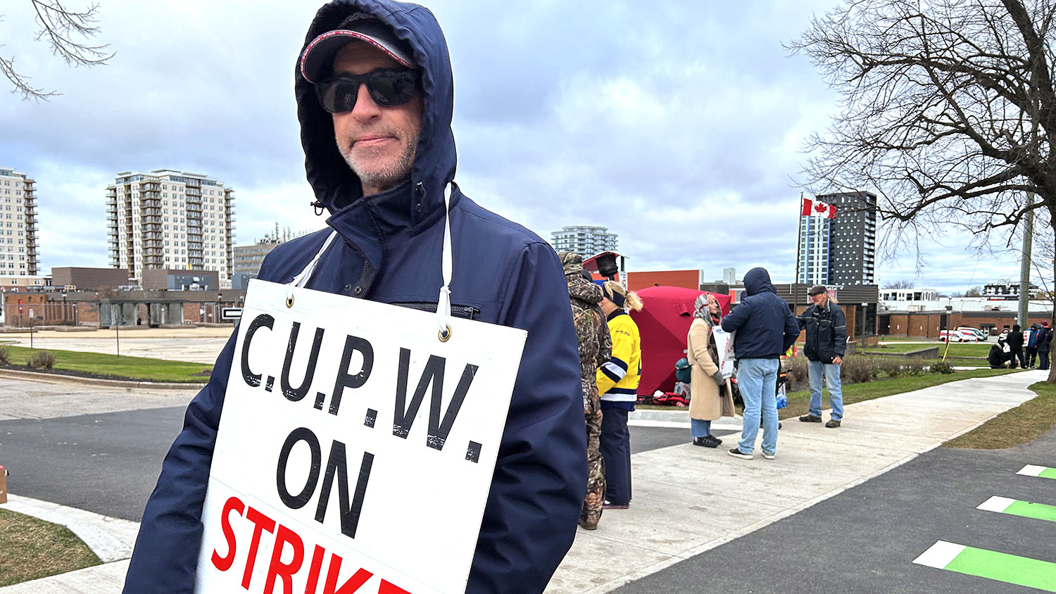 Man wearing strike sign that says "C.U.P.W. ON STRIKE"