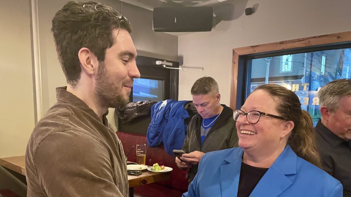 A woman smiles while speaking with a man in a crowded room